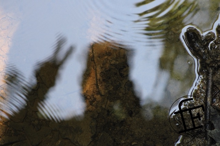 rippling water with a reflection of someone showing a peace sign.